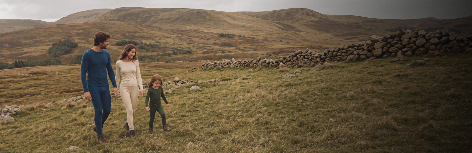 A wide shot captures a family of three walking through a sprawling, grassy field. The expansive natural landscape features rolling hills in the distance under a pale sky.