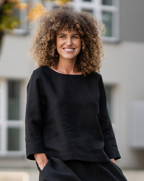 Woman wearing a black linen blouse standing outdoors with blurred background