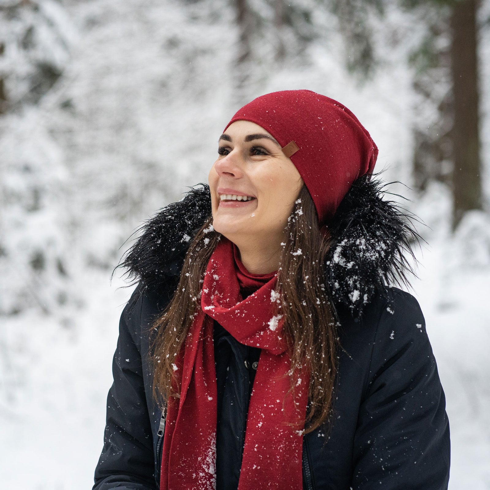 Woman wearing a red beanie and scarf in a snowy forest