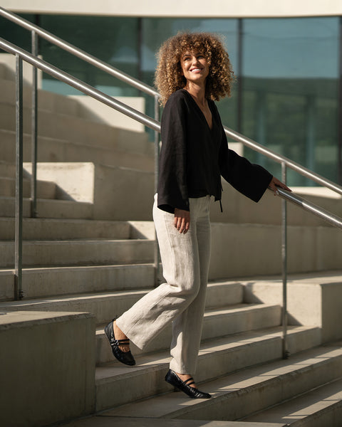 Woman walking up a set of stairs outdoors wearing black linen shirt thea and natural linen trousers