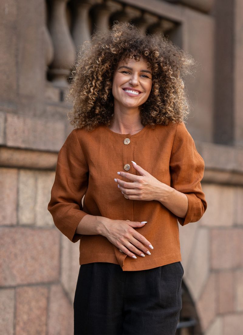 Woman wearing a brown jacket standing against a stone wall.
