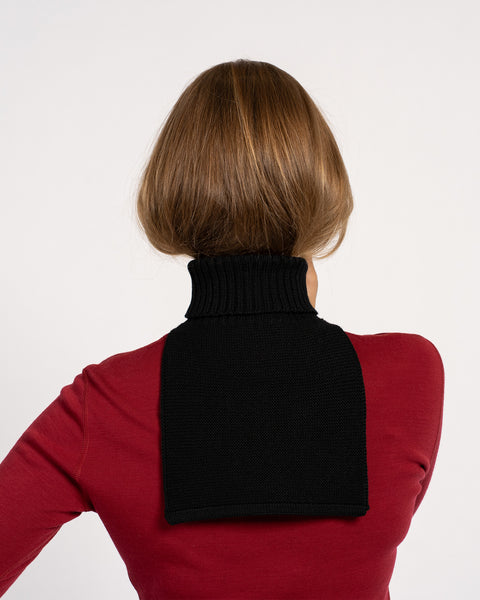 Back view of a woman wearing a black knitted merino wool dickie neck warmer over a red top.