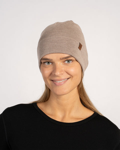 Woman wearing a creamy beige knitted Merino wool beanie, front view, smiling.