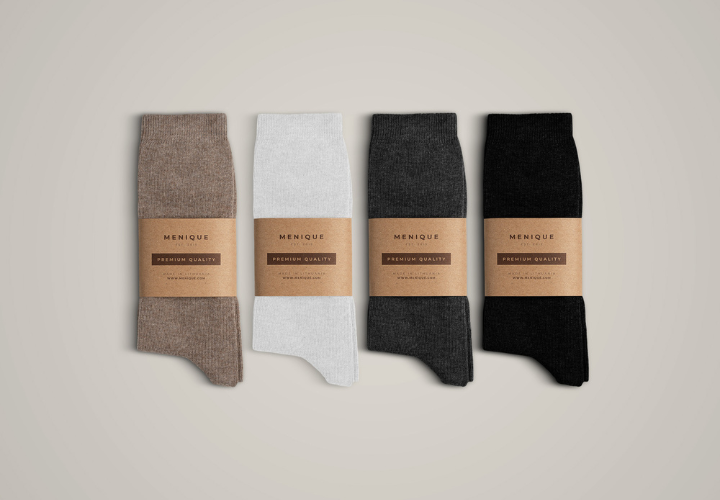 Four pairs of menique merino wool socks in brown, white, dark gray, and black, neatly folded with eco-friendly kraft paper labels.