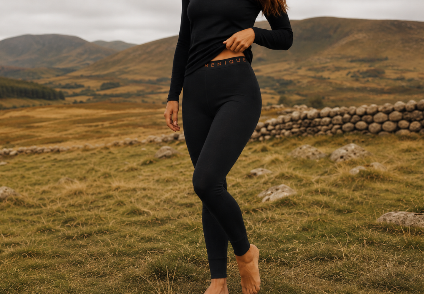 A person standing barefoot in a grassy, hilly landscape wearing a black long-sleeved base layer set.