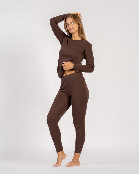 Full-body shot of woman in brown merino wool thermal set, one hand raised.