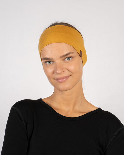 Smiling woman in yellow merino headband with visible logo tag, paired with black top – front portrait.