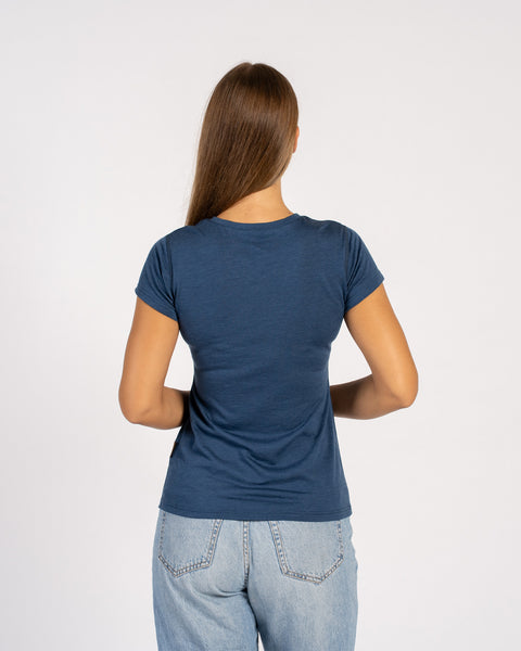 A back view of a woman in a blue t-shirt and jeans, with her arms resting straight down at her sides.