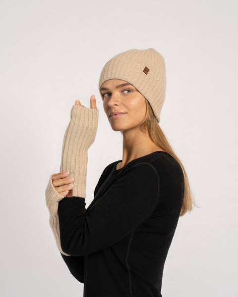 Frontal pose of the model wearing creamy-beige wrist gloves and beanie, one hand touching the other forearm.