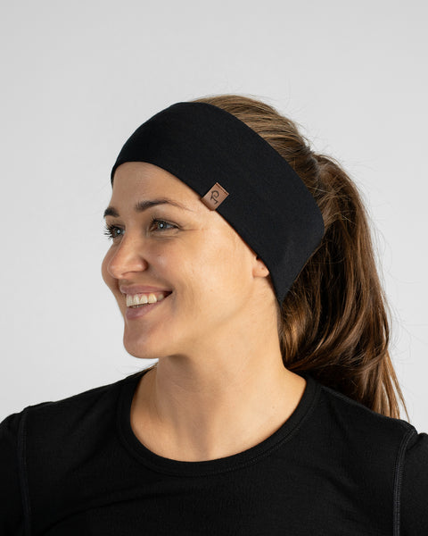 A smiling woman with her hair pulled back into a ponytail, wearing a black long-sleeve top and a wide black knit headband while looking to the side.