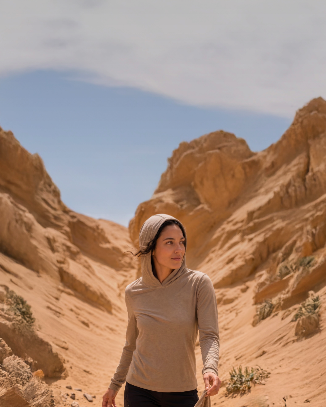 A woman wearing a lightweight, beige long-sleeve sun hoodie walking through a narrow, sandy desert canyon.
