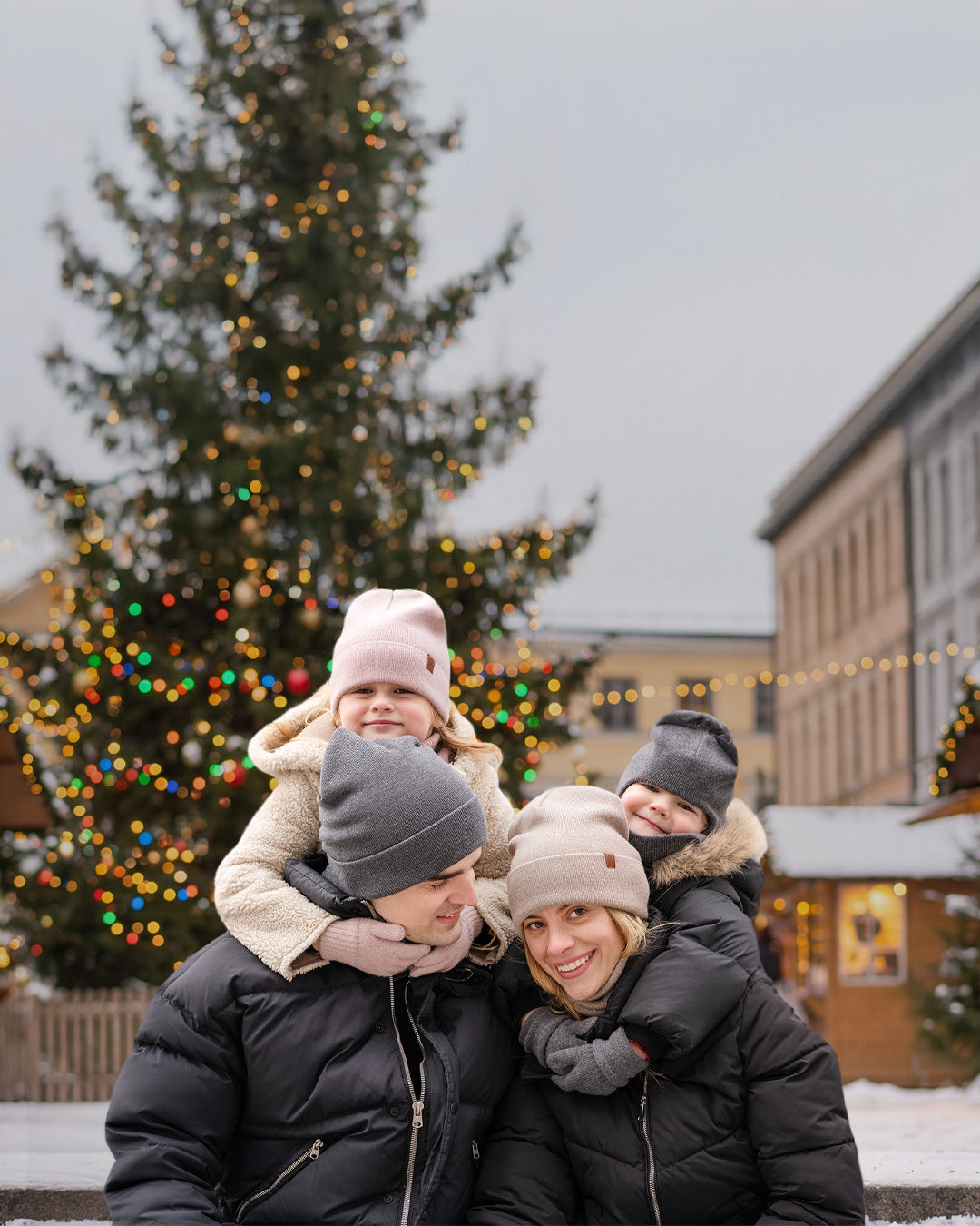 Family of four posing outdoors with a decorated Christmas tree in the background