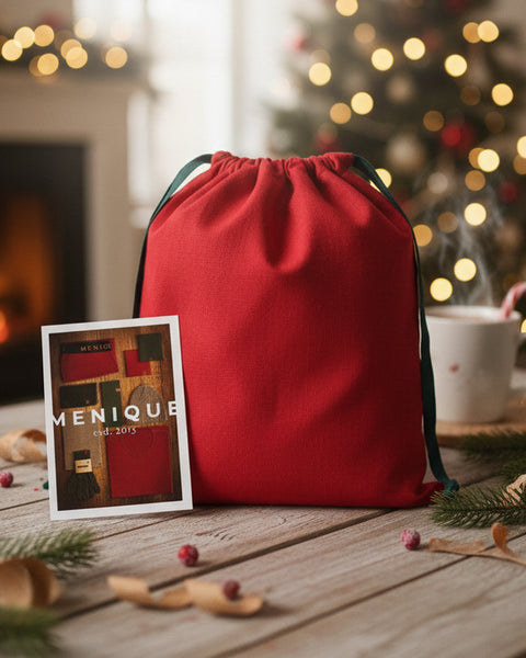 Red drawstring bag on a wooden table with a Christmas tree and fireplace in the background