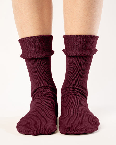 A straight-on view shows a person from the mid-thigh down, wearing ribbed, royal cherry color socks with a folded-down cuff. The socks extend to the mid-calf, and the person&#39;s feet are positioned slightly apart on a plain white background. The lighting is uniform, highlighting the texture and folds of the socks.
