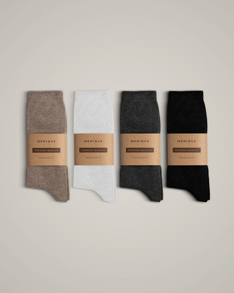 Four pairs of ribbed socks laid out neatly side-by-side on a plain, light grey background. Each pair is wrapped in a brown kraft paper band that reads "MENIQUE" with "PREMIUM QUALITY" printed below it.