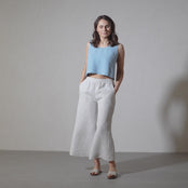 A woman with shoulder-length brown hair models a cloudy blue linen sleeveless crop top and wide-legged linen menique pants, turning slowly and posing in a short video against a simple studio background.