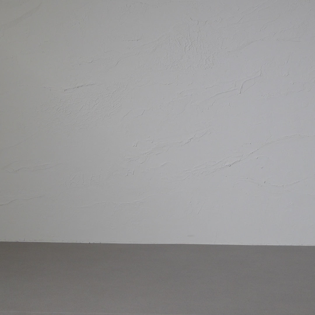 A woman with long, curly brown hair smiles and models a sleeveless, dark green maxi linen dress against a textured gray backdrop in a short video. They turn to the side, showing the flow of the dress.