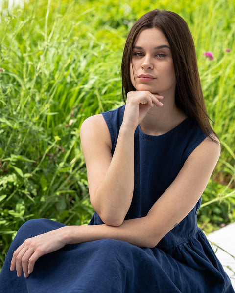 Young woman posing in a city, sitting on the ground, wearing linen smock dress Maya in a Storm blue cover.